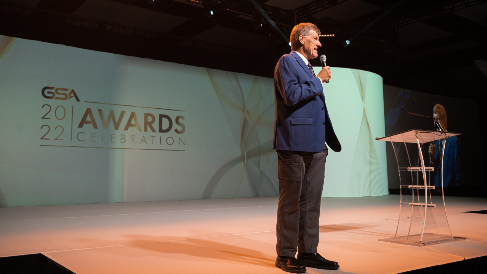 an image of a presenter on stage with the Awards Dinner styled background screen