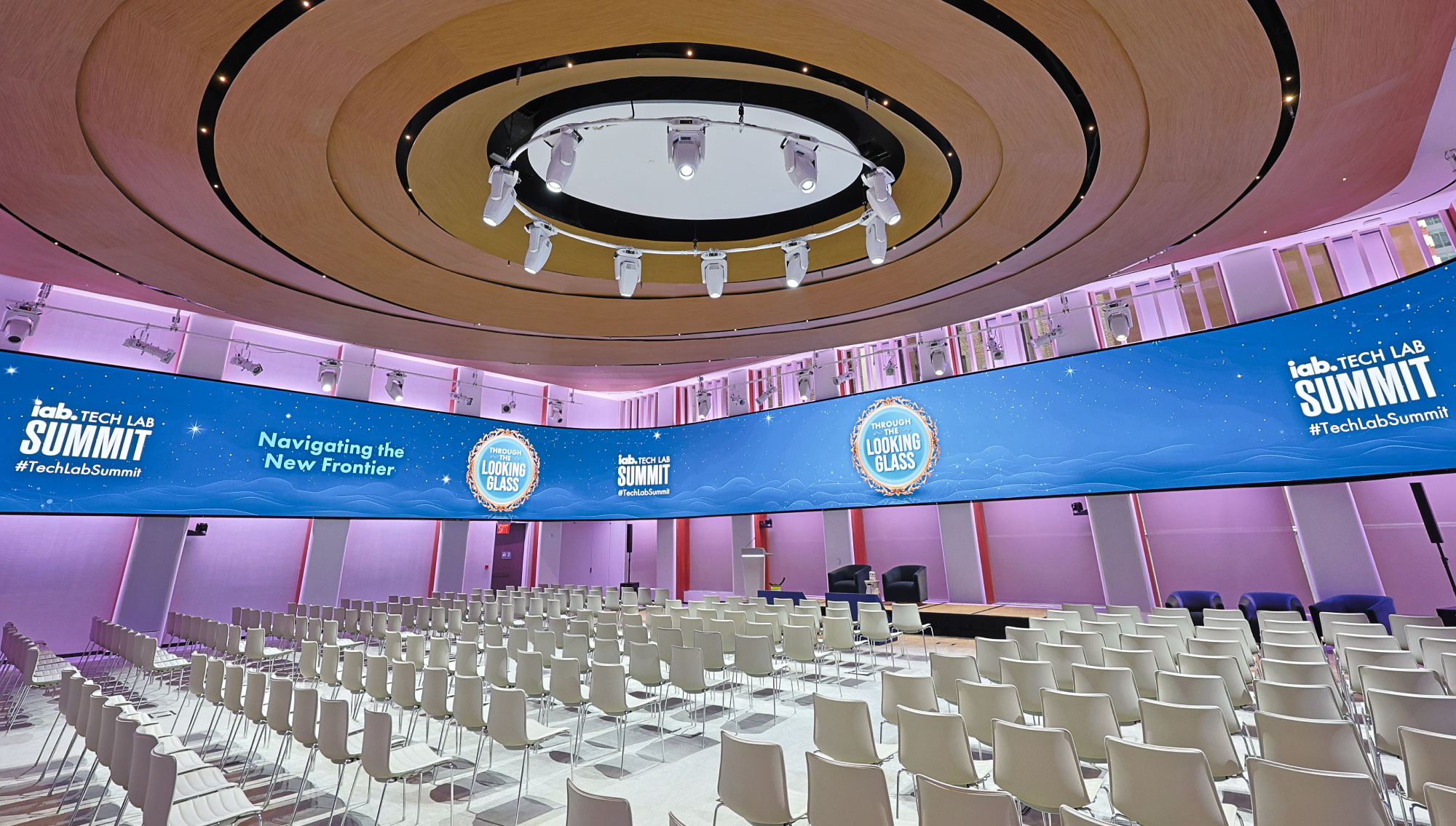 Conference room stage and chairs with video screen wrapping the room with "Through the Looking Glass" and IAB Tech Lab Summit logos